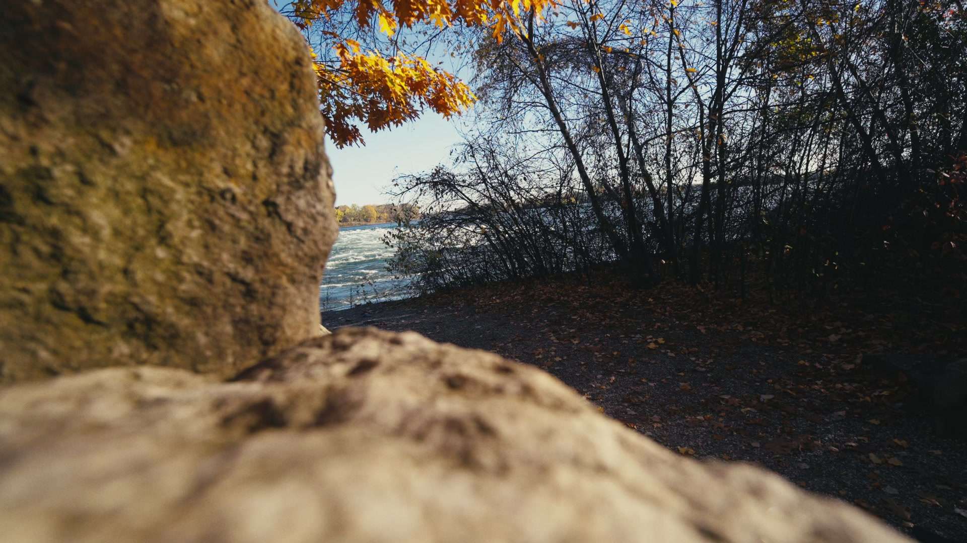 Guillaume Dubois marche entre les rochers au bord d’un fleuve, au Canada, en automne