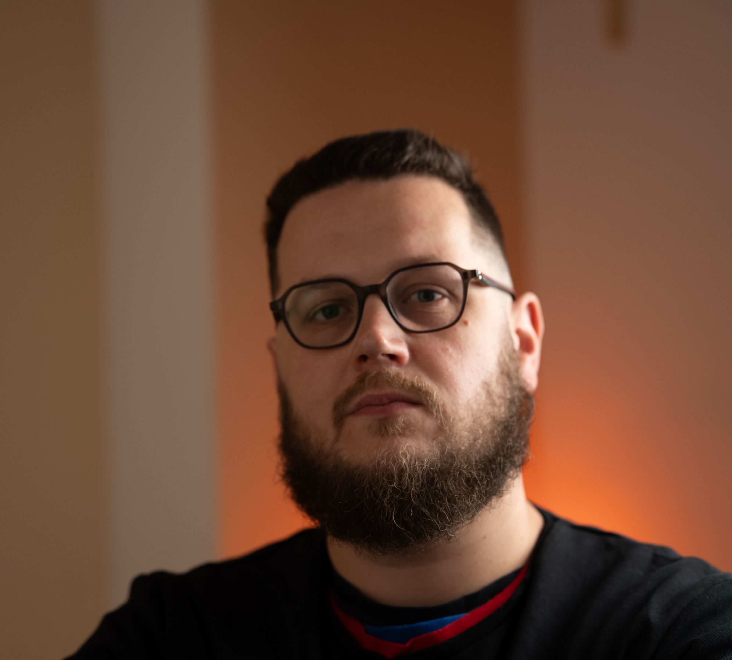 Portrait de Guillaume Dubois, réalisateur, barbe et lunettes, devant un mur éclairé d'une lumière chaude
